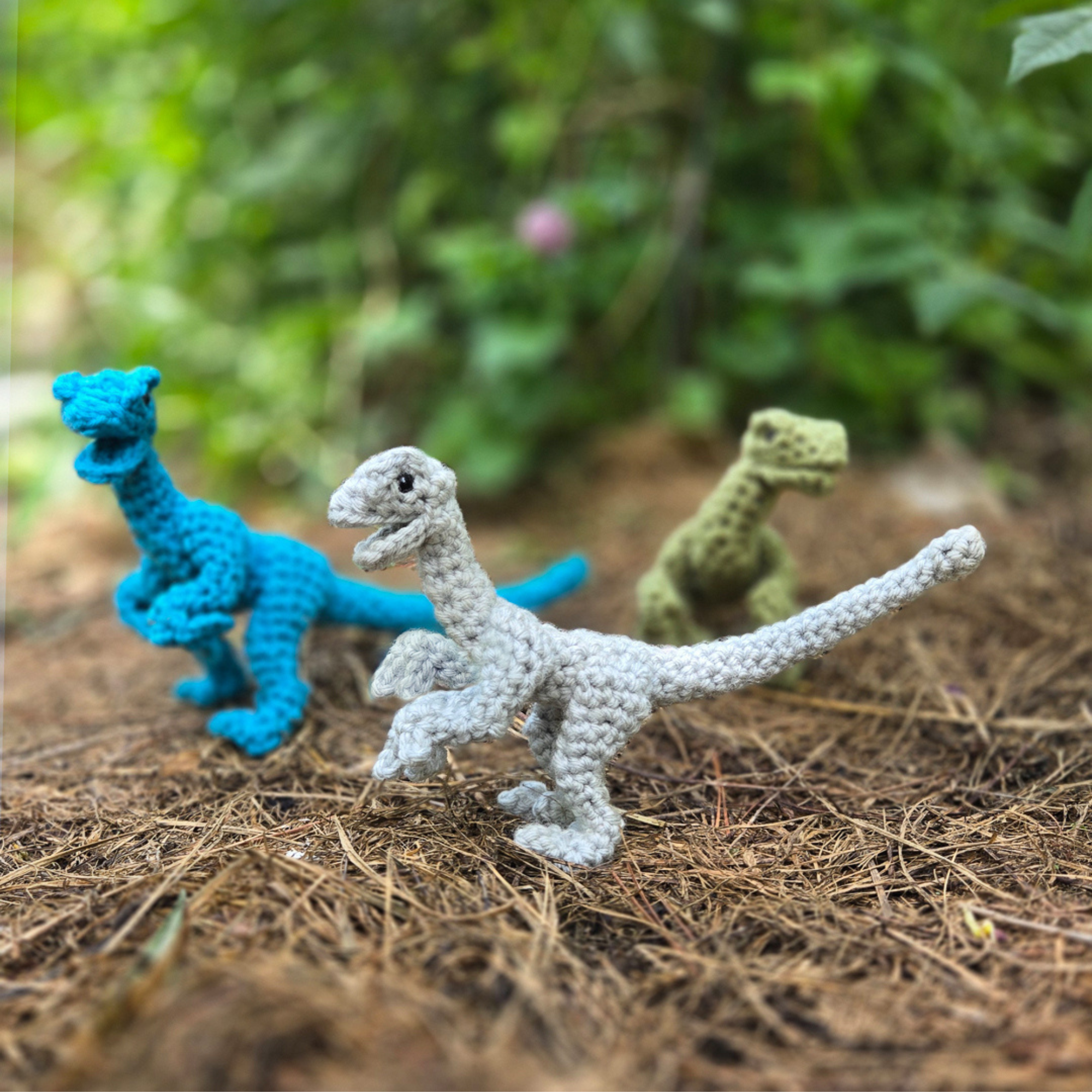 3 crochet raptor dinosaurs in a natural setting.