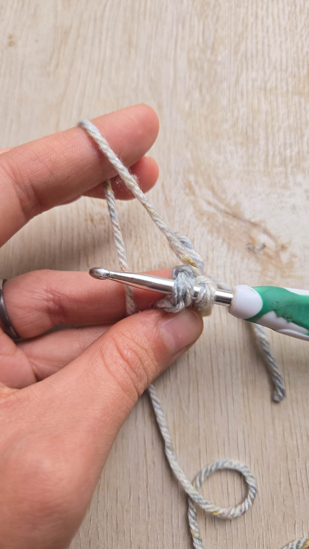 a hand holding grey yarn and a crochet hook