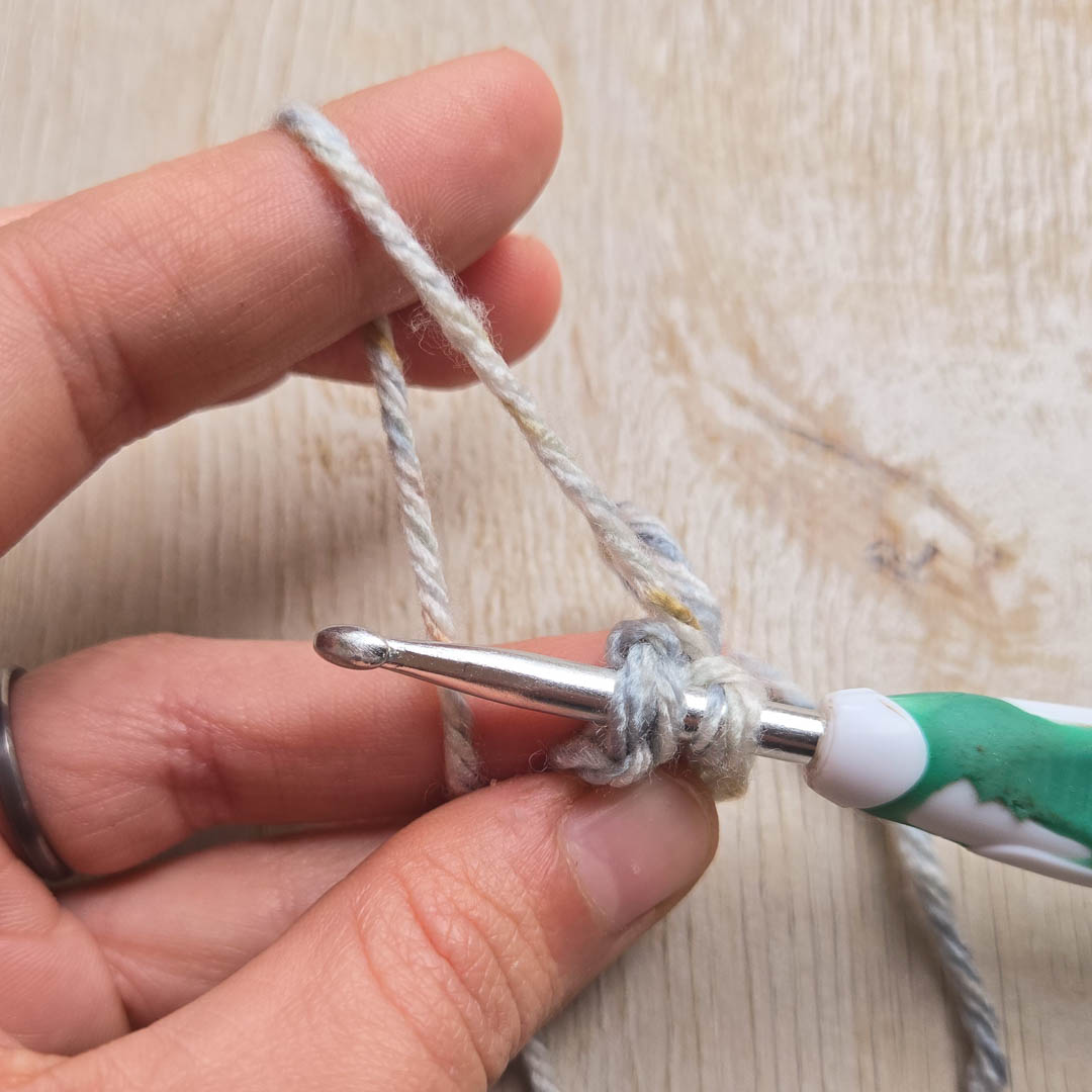 Fingers and a crochet hook working with grey yarn.