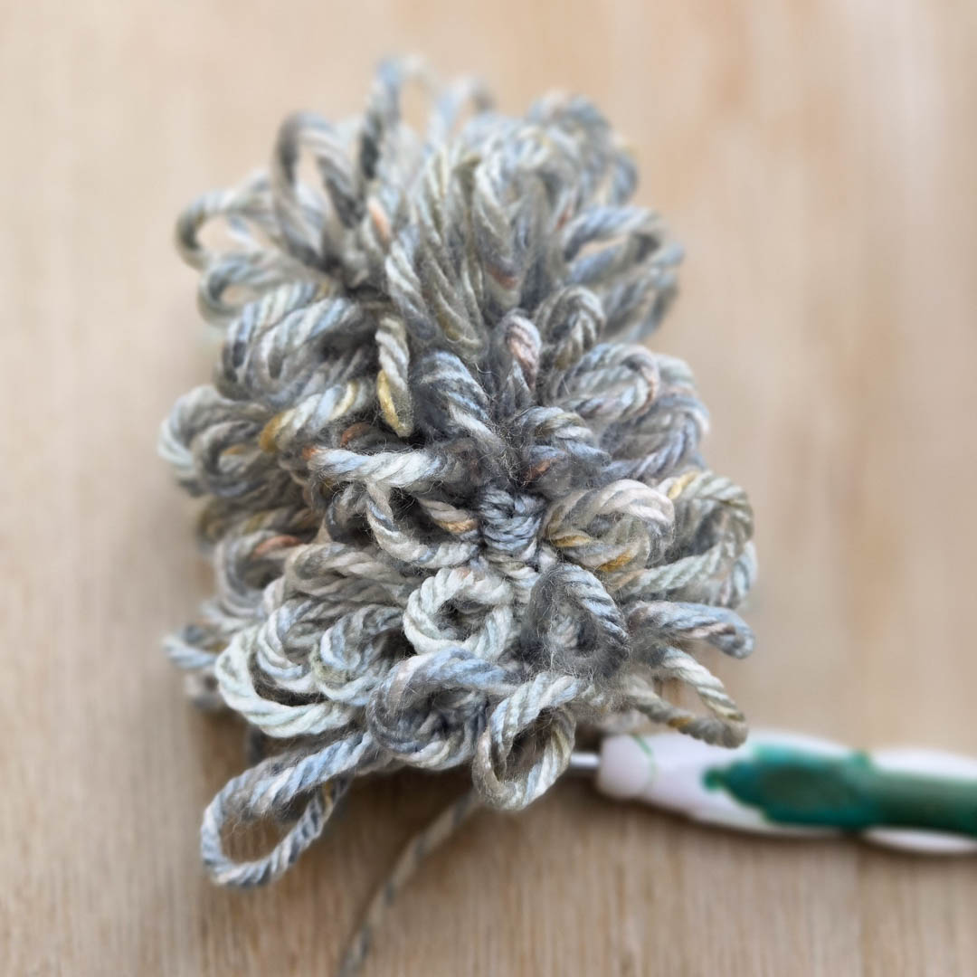 Fingers and a crochet hook working with grey yarn.