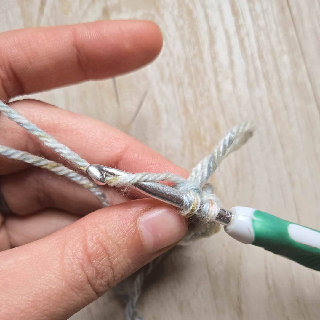 A crochet hook pulling yarn through stitches to complete a crochet loop stitch.