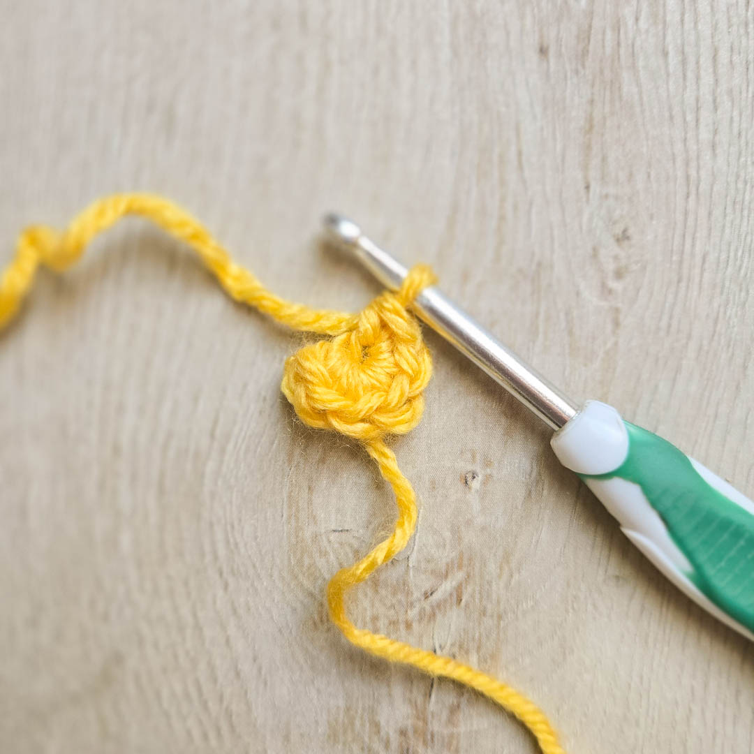 A crochet magic circle with a crochet hook, the start of the daffodil crochet pattern.