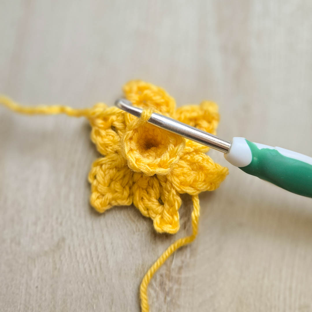 A yellow crochet flower in the works with a crochet laying on the petals.