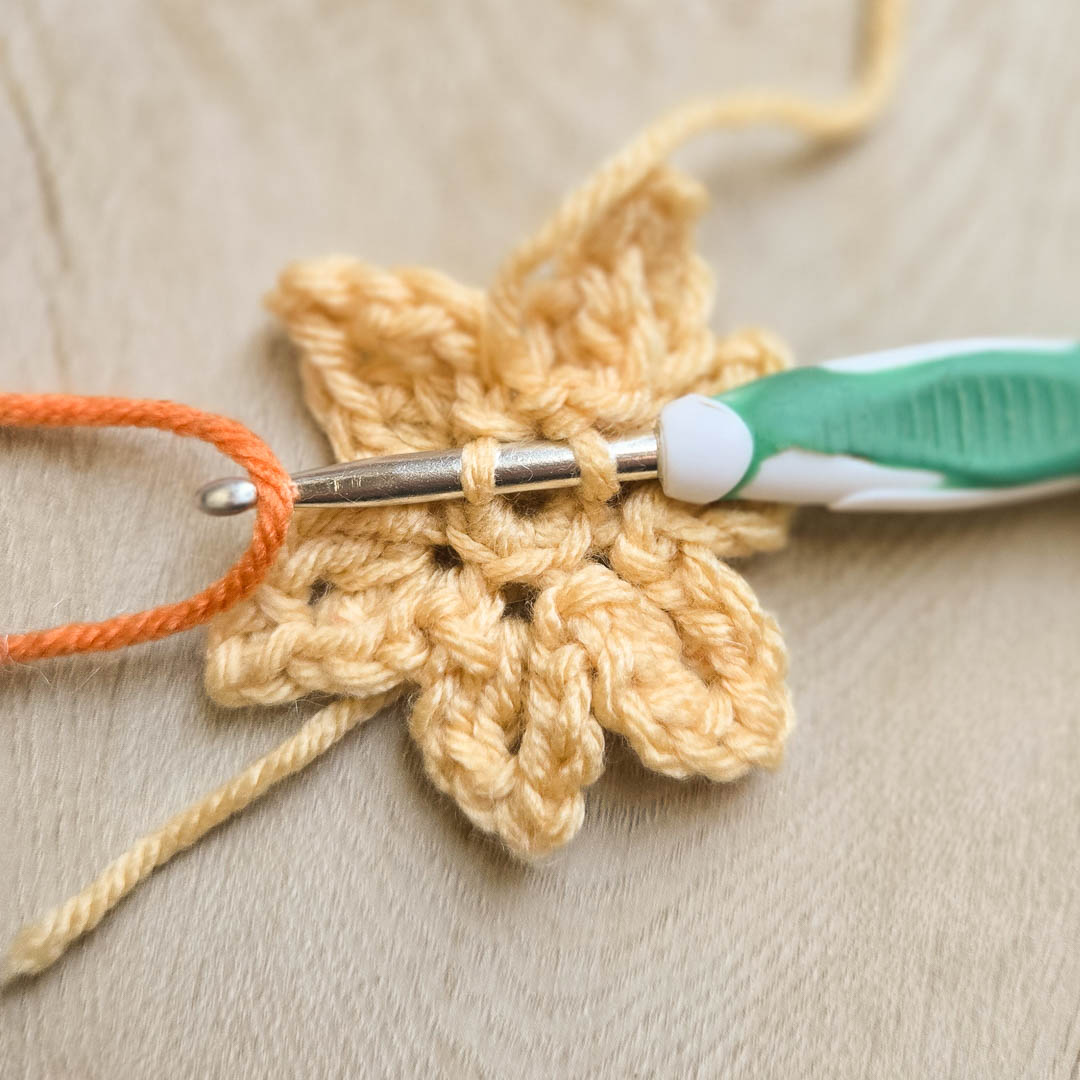 Crocheting orange yarn through a yellow stitch to make a multi-colored crochet flower.