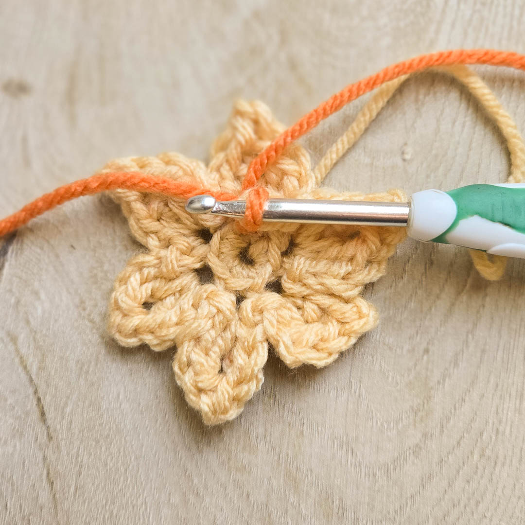 Orange yarn attached to the petals of a crochet daffodil.