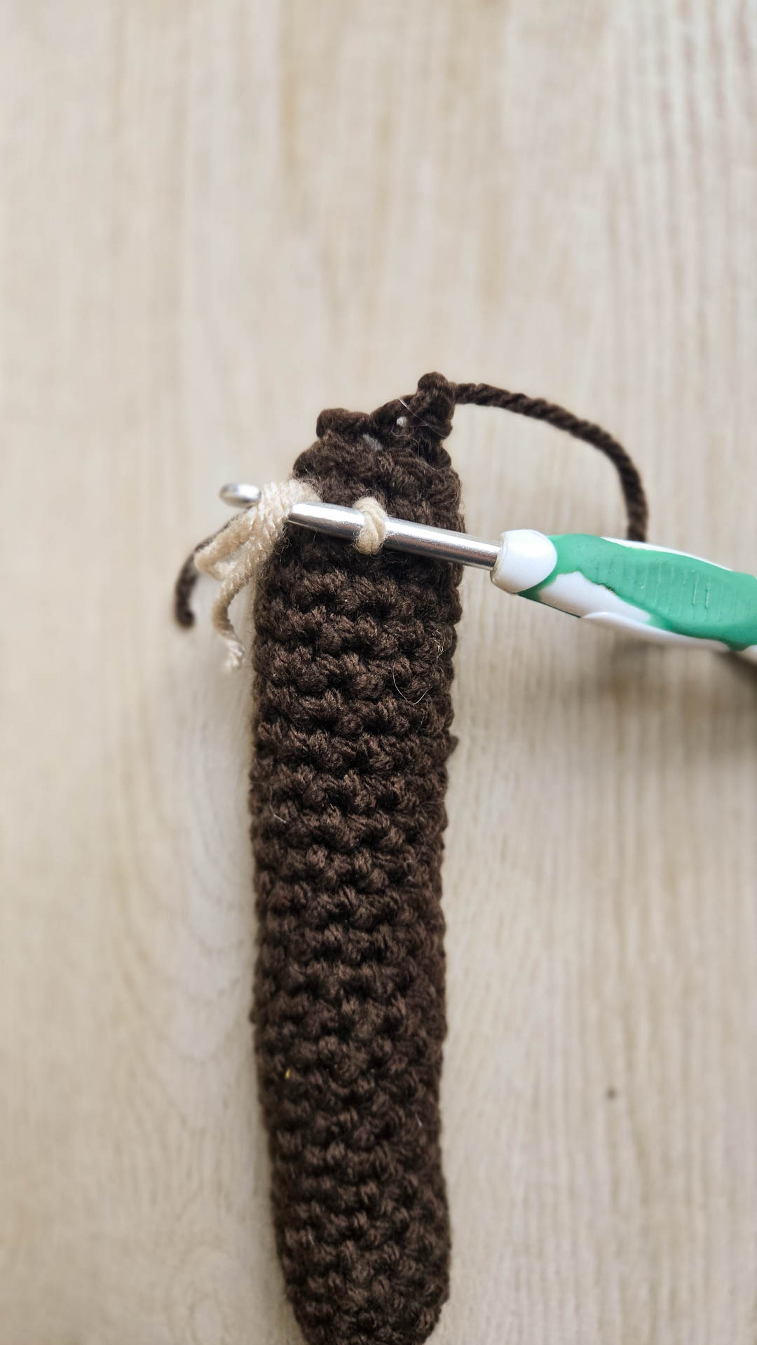 A crochet hook tying a short yarn thread to another crochet object.