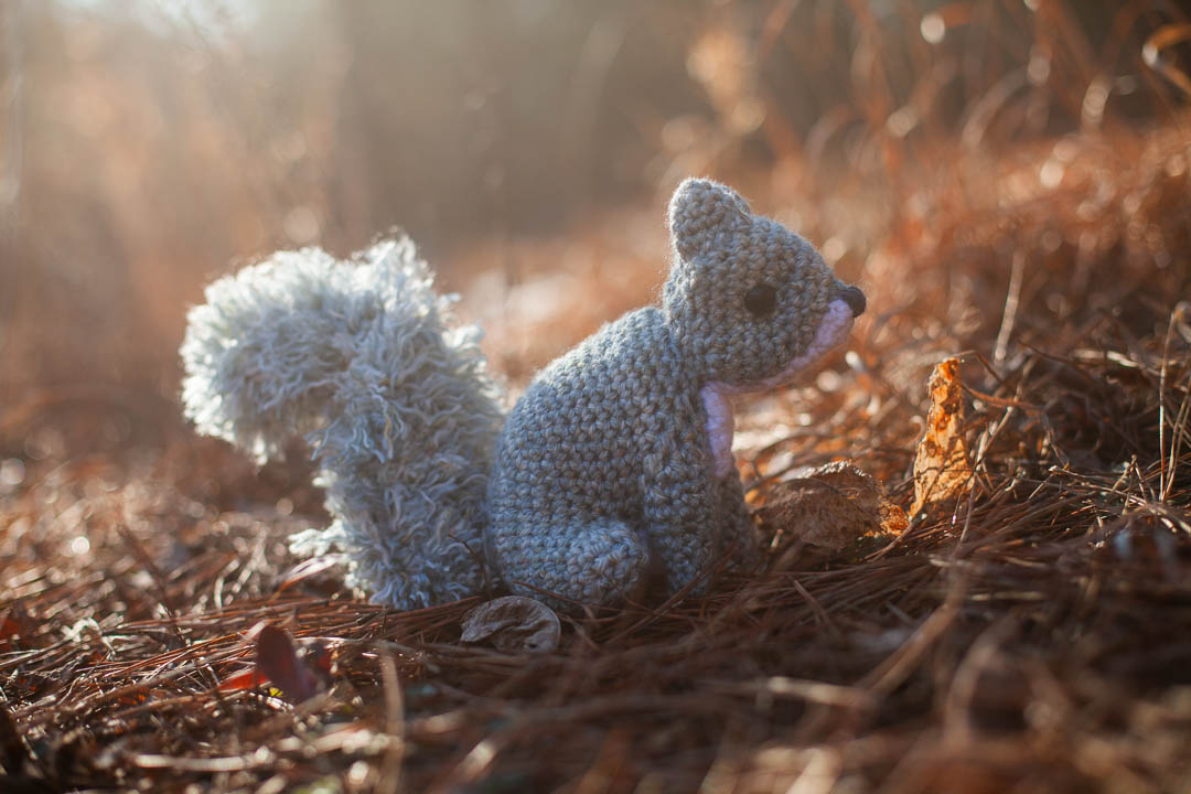 A grey crochet squirrel with sunlight filtering behind it.