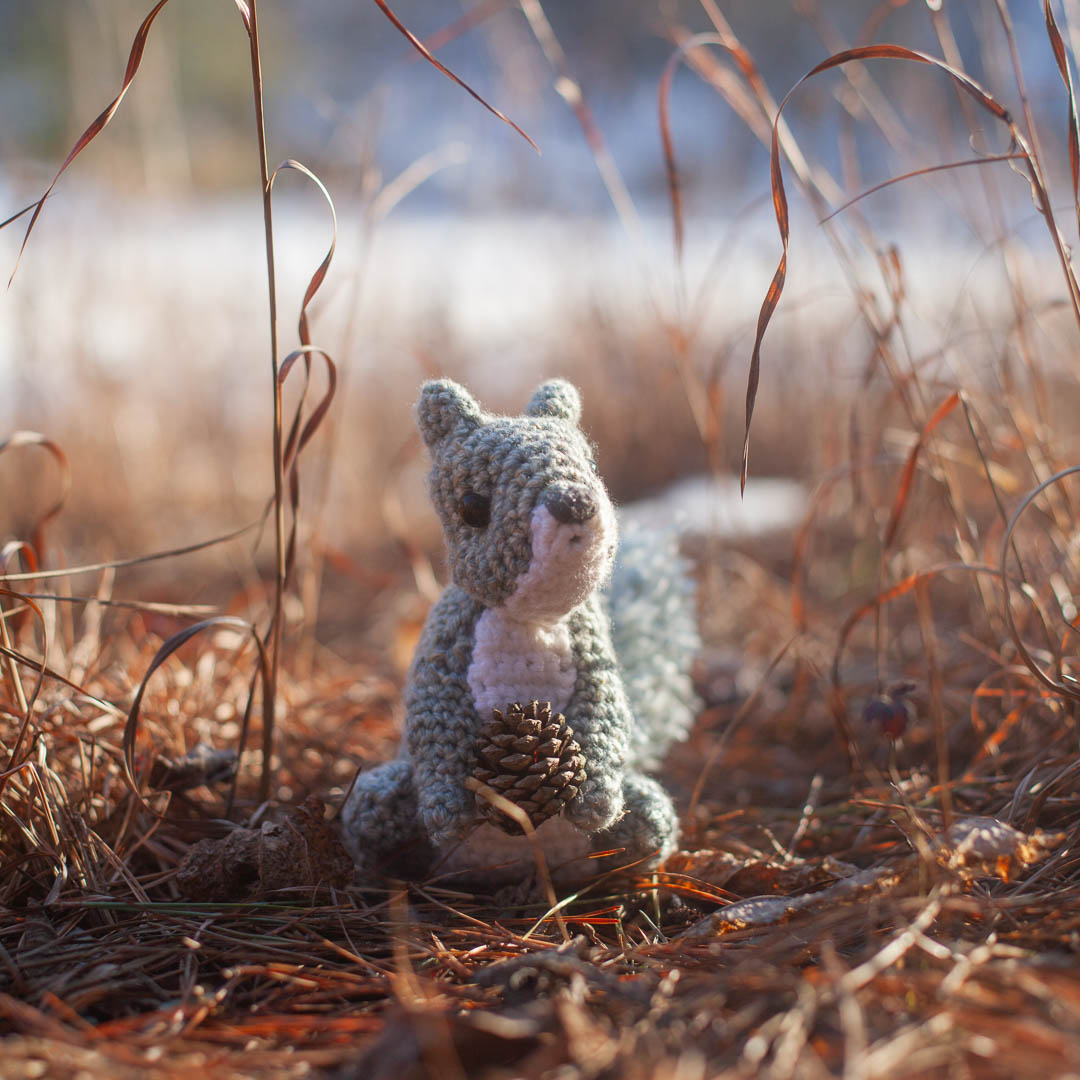A crochet squirrel holding a pinecone.
