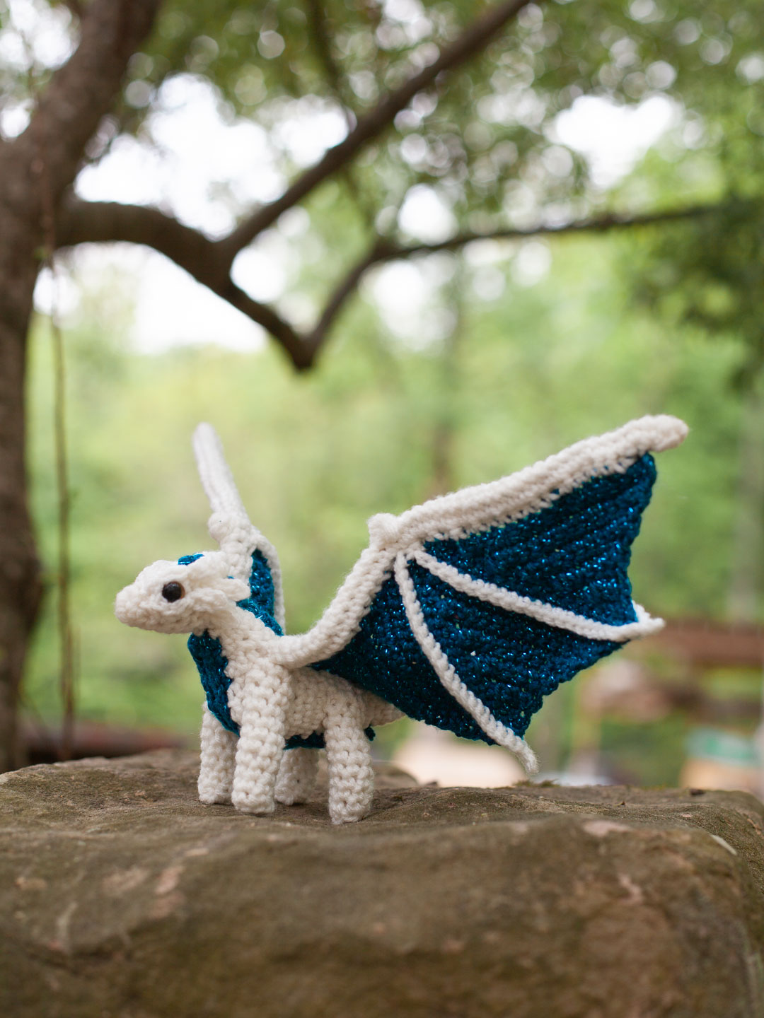 Little Dragon Crochet Pattern a white and blue crochet dragon perched on a rock.