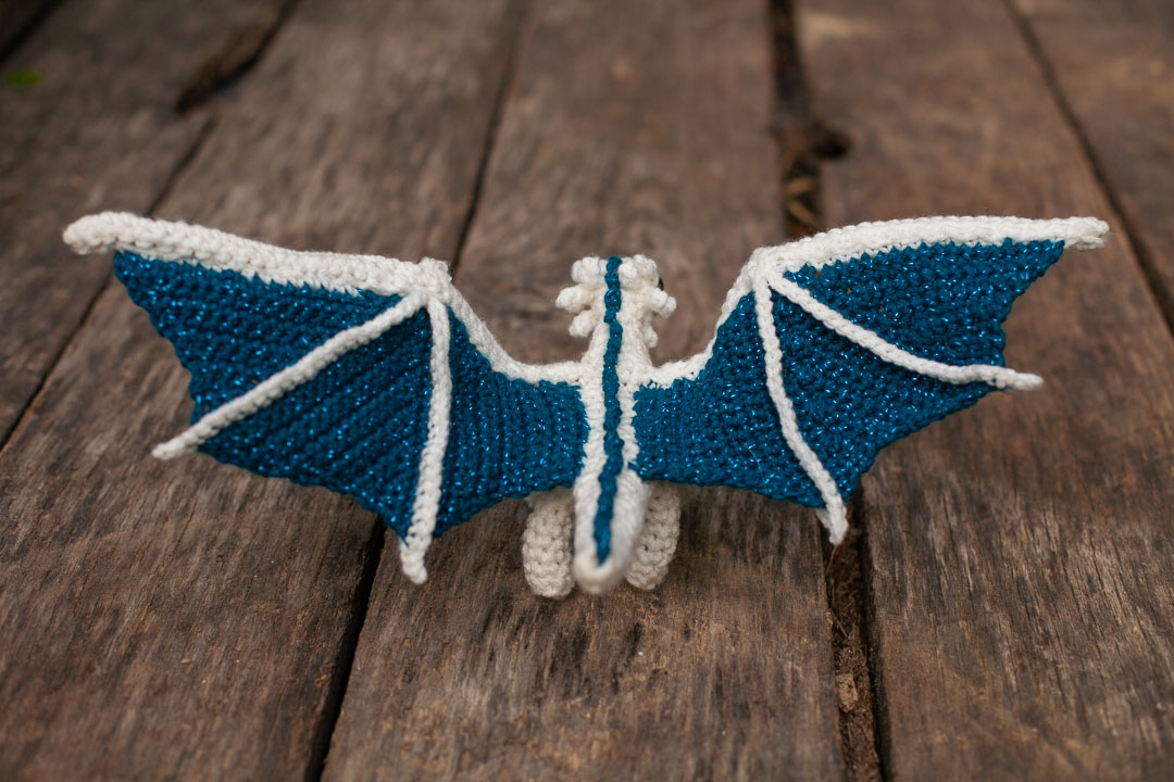 A rear view of a dragon with it's wings spread wide on a wooden background.